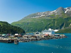 there is a boat docked in the water next to a mountain side town with snow covered mountains behind it