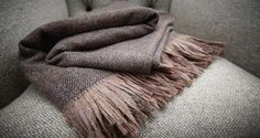 a brown and black blanket sitting on top of a chair next to a gray pillow