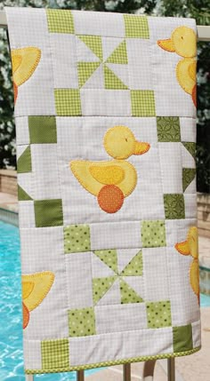 a quilted wall hanging next to a swimming pool with ducks and squares on it