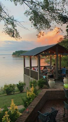 a gazebo sitting on top of a lush green field next to the ocean at sunset