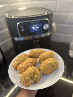 a person holding a white plate with food on it in front of an air fryer