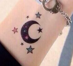 a person with a tattoo on their wrist holding onto a keychain that has stars and a crescent