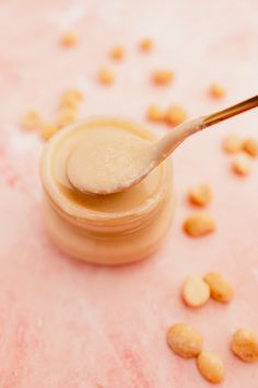 a spoon full of peanut butter sitting on top of a pink surface with peanuts scattered around it