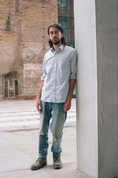 a man with long hair standing next to a tall pillar in front of a building