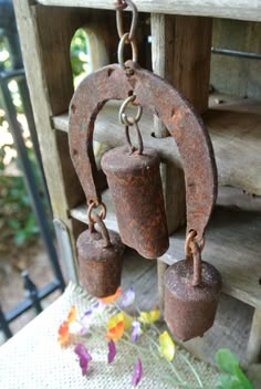 two rusty bells hanging from a chain on a porch with flowers in the foreground