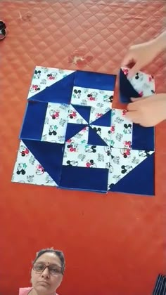 someone is making a mickey mouse quilt on the table with their hand over it and another person holding something in front of them