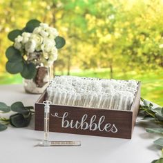 a wooden box filled with white candles next to flowers and greenery on top of a table