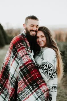 a man and woman wrapped in a blanket smile at the camera while standing next to each other