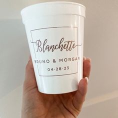 a person holding up a white cup with brown lettering