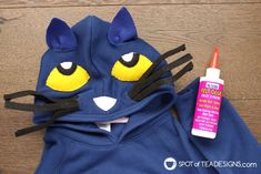 a blue cat hoodie with yellow eyes and black ears next to a bottle of glue