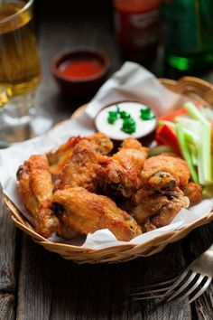 a basket filled with chicken wings next to a glass of beer and some veggies