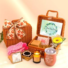 a wicker basket with flowers, candles and other items in it sitting on a white surface