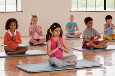 a group of children sitting on yoga mats in a room with their hands clasped together