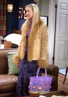 a woman standing in front of a brown couch holding a purple bag and wearing a fur coat