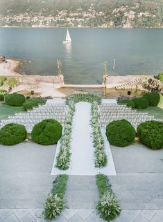 an outdoor ceremony setup with white chairs and greenery on the ground next to water