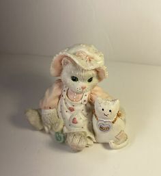 a white cat figurine sitting next to a teddy bear on a white surface