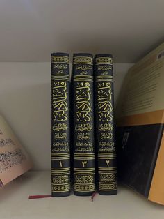 three books are sitting on a shelf next to an open book with arabic writing in gold and black