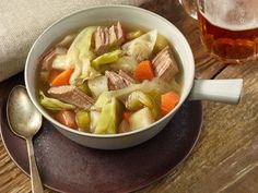 a bowl of soup with carrots, celery and meat on a table