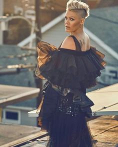 a woman in black dress standing on top of a roof with her hands behind her back