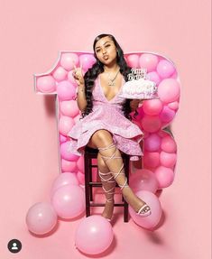 a woman sitting on a chair with a cake in front of her, surrounded by balloons