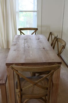 a wooden table with chairs around it and a window in the back ground behind it