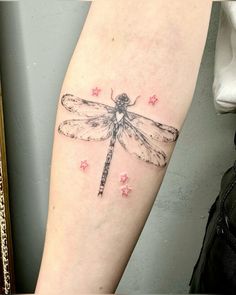 a small dragonfly tattoo on the right arm and leg, with pink stars around it