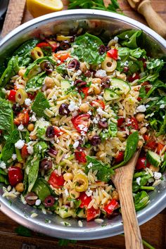 a bowl filled with pasta salad next to a wooden spoon and lemon wedges on the side