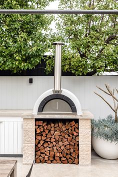 an outdoor pizza oven with firewood in the center and potted plants next to it