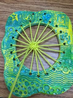 a close up of a green and yellow object on a wooden table with yarn in the middle