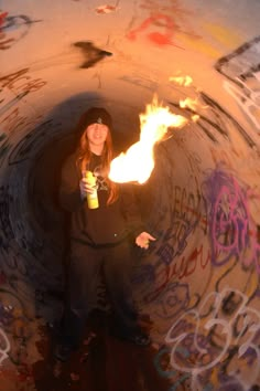 a woman standing in a tunnel holding a drink and fire stick with graffiti on it