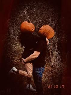 a man and woman wearing pumpkins on their heads walking through the woods with each other