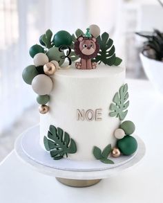 a white cake decorated with green leaves and a lion on top that says noe