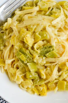 a white plate topped with pasta covered in cheese and vegetables next to a silver fork