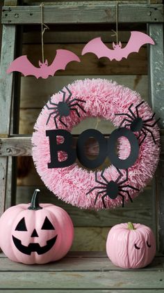 a pink wreath with bats on it next to two pumpkins and a boo sign