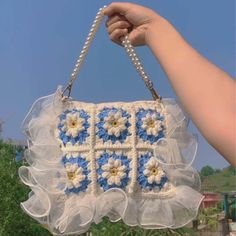 a hand holding a blue and white purse with flowers on it's front flap