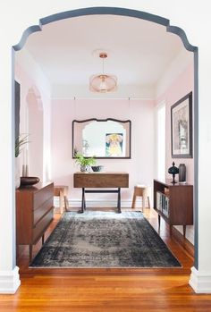 a living room with pink walls and wood flooring is seen through an arch in the doorway