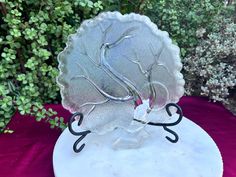 a frosted glass tree on top of a white plate with black metal wire around it