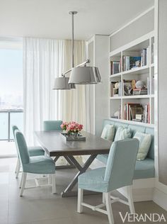 a dining room table with blue chairs next to a book shelf and bookshelf