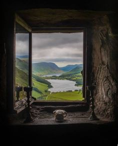 an open window in a stone building with the view of mountains and lake from inside