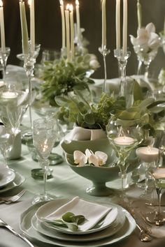 Elegant dining table set with white candles, crystal glassware, and green floral centerpieces.