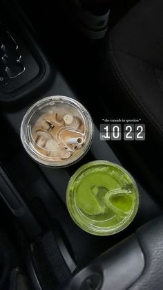 two plastic cups filled with green liquid sitting on top of a black car dash board