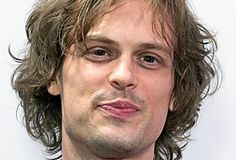 a close up of a person wearing a suit and tie with his hair pulled back