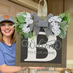 a woman holding up a sign that says welcome to our home with flowers on it