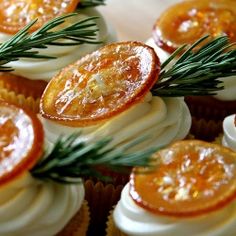 cupcakes with orange slices and rosemary sprigs on top are arranged in rows