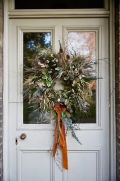 a wreath on the front door of a house with an orange ribbon hanging from it