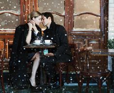 a man and woman sitting at a table in front of a window covered with snow