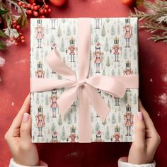 a woman's hands holding up a wrapped gift box with pink ribbon and bows