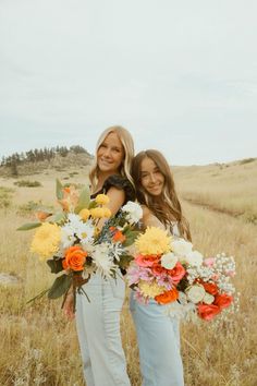 two beautiful young women standing next to each other in a field with flowers on their arms