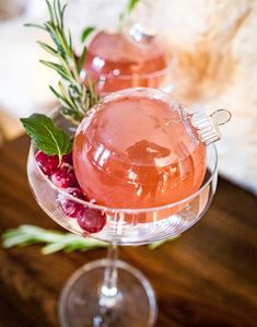 two glasses filled with liquid and garnished with berries on a wooden table top