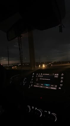 the dashboard of a car at night with lights in the distance and dark clouds overhead